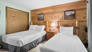 Une chambre avec deux lits simples, des lambris en bois sur les murs, une porte et une table de chevet avec une lampe.