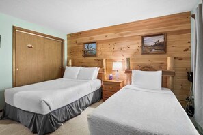 Ein Zimmer mit zwei Einzelbetten, Holzvertäfelung an den Wänden, einer Tür und einem Nachttisch mit Lampe.