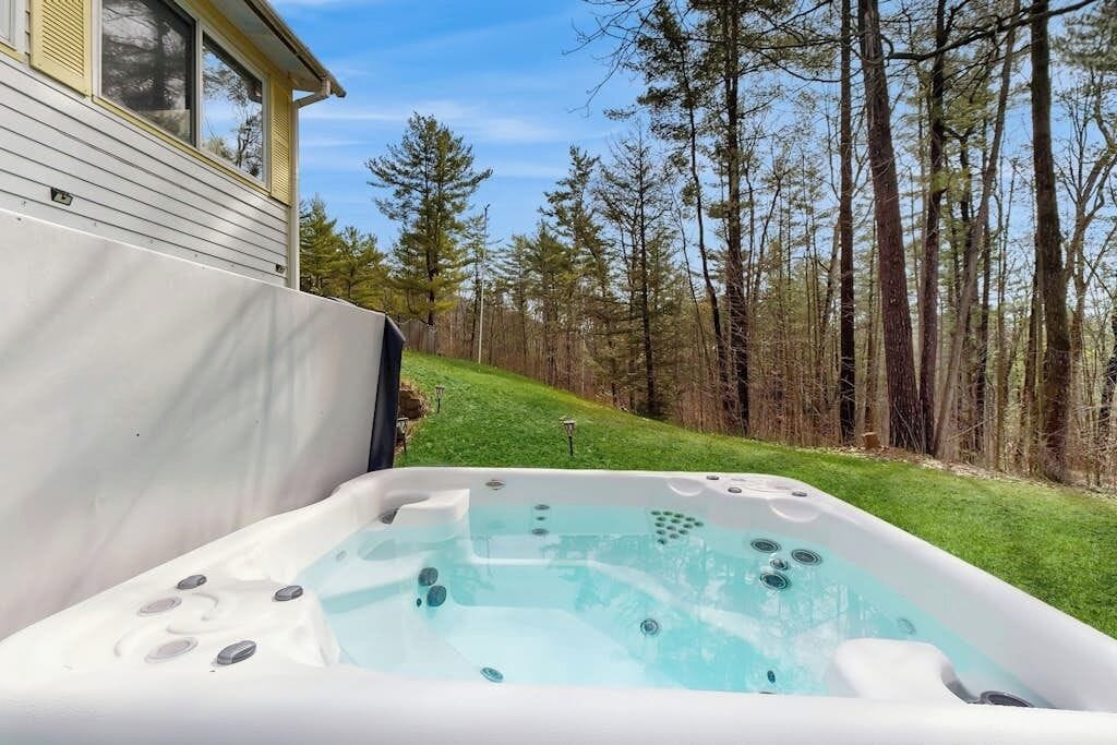 Ein Whirlpool im Garten mit einem Haus und einem Wald im Hintergrund.