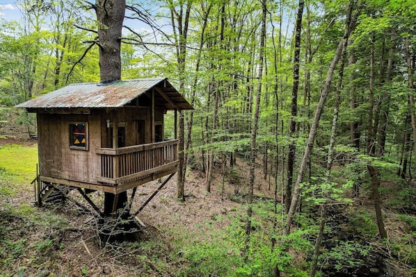 A wooden treehouse with a balcony, surrounded by a forest.