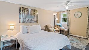 Une chambre d’hôtel avec un lit, une chaise, une lampe, un tableau, une horloge et un ventilateur de plafond.