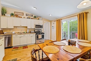 Una cocina con armarios blancos, microondas, estufa y una mesa de comedor con individuales.