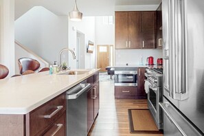 A modern kitchen with a central island, stainless steel appliances, and wooden cabinets. - 3BR scenic adventure pad with game room (Lake George)