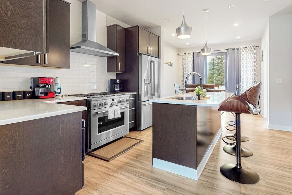 A modern kitchen with dark cabinetry, a stainless steel refrigerator, and a central island with bar stools.