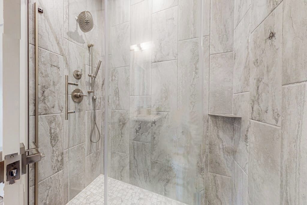 Eine begehbare Dusche mit Glastür, gefliesten Wänden und einer Handbrause.