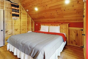 Un dormitorio de cabaña de madera con una cama, un armario y una pared roja.