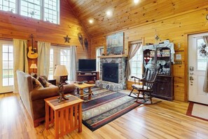 Interior acogedor de una cabaña con techo de madera, chimenea, televisor y una mecedora.