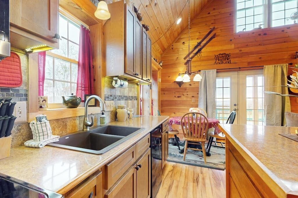 Una cocina con armarios de madera, un lavamanos y un comedor con una silla.