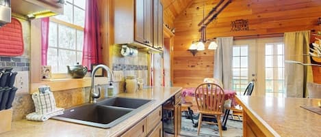 Una cocina con armarios de madera, un lavamanos y un comedor con una silla.