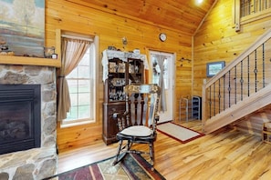 A wooden interior with a stone fireplace, a wooden chair, and a staircase.