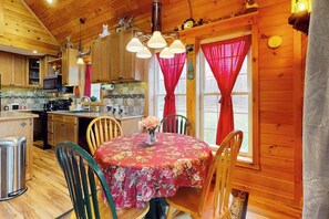 Interior de una cabaña de madera con una mesa de comedor, sillas y una zona de cocina.