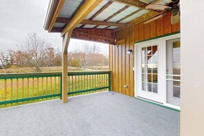 A covered porch with a green railing, a white door, and a view of a grassy area with trees.