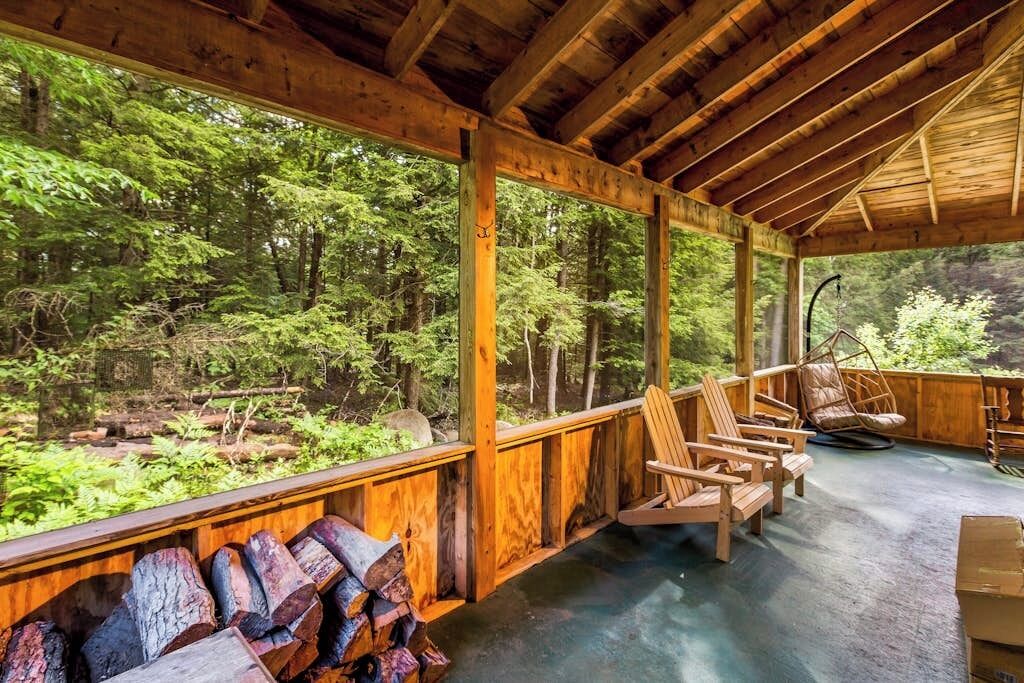 Ein überdachter Außenbereich mit Holzstühlen, einer Hängematte und Blick auf einen Wald.