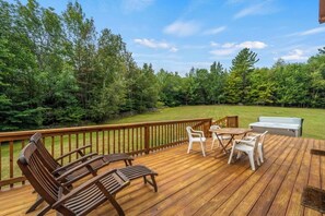 A wooden deck with outdoor furniture, a barbecue grill, and a view of a forested area. - Quiet 4BR Adirondacks Dog Friendly - Hot Tub (Johnsburg)