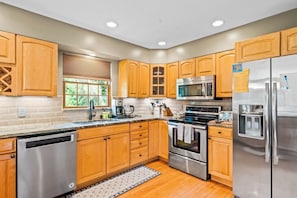 A modern kitchen with wooden cabinets, stainless steel appliances, and a built-in dishwasher. - Quiet 4BR Adirondacks Dog Friendly - Hot Tub (Johnsburg)