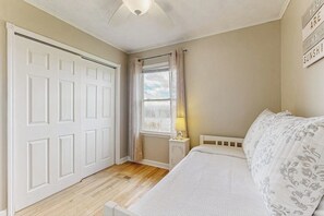 Ein Schlafzimmer mit einem Bett, einem Nachttisch, einem Fenster mit Vorhängen und einer Tür.