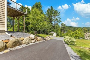 Une allée menant à une maison, avec une terrasse en bois, un mur de pierres et un ciel dégagé.
