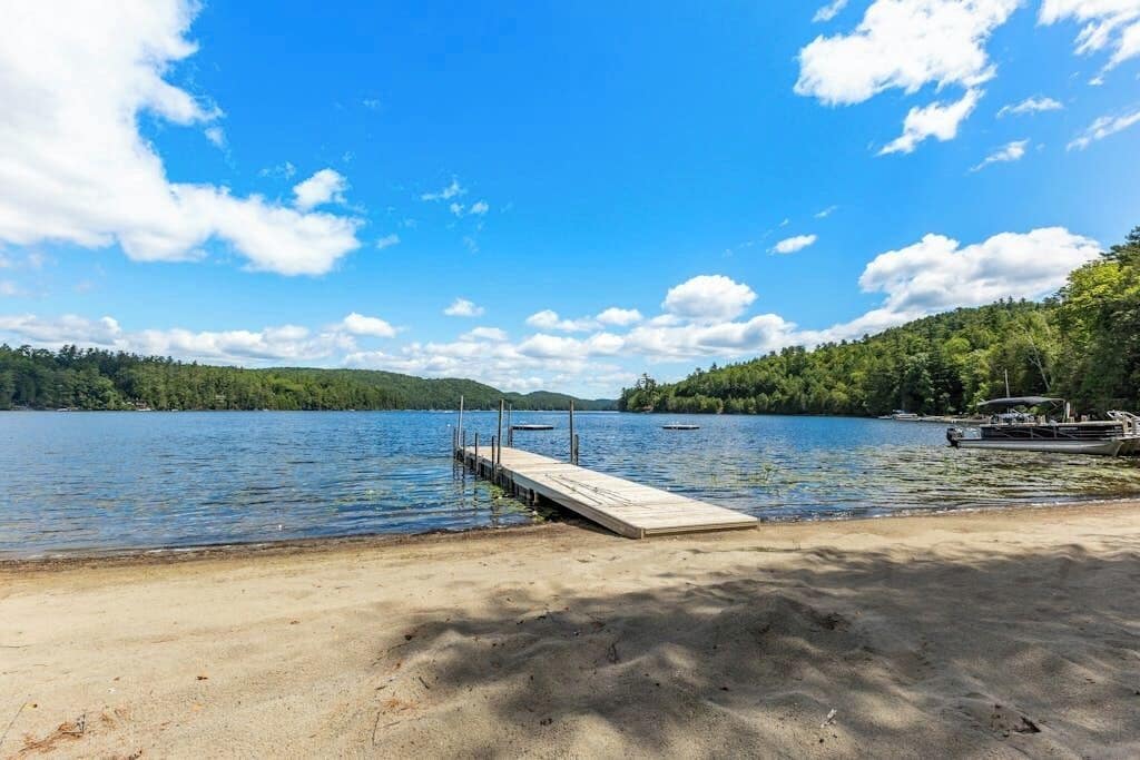 A lake with a wooden dock extending into the water, surrounded by trees and hills.