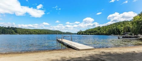 A lake with a wooden dock extending into the water, surrounded by trees and hills.