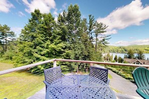 Una terraza con mesa y sillas que da a un lago y un bosque.