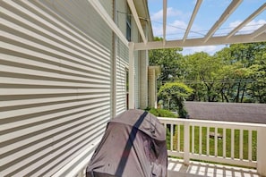Une véranda couverte avec un barbecue, des rampes blanches et une vue sur un quartier résidentiel arboré.