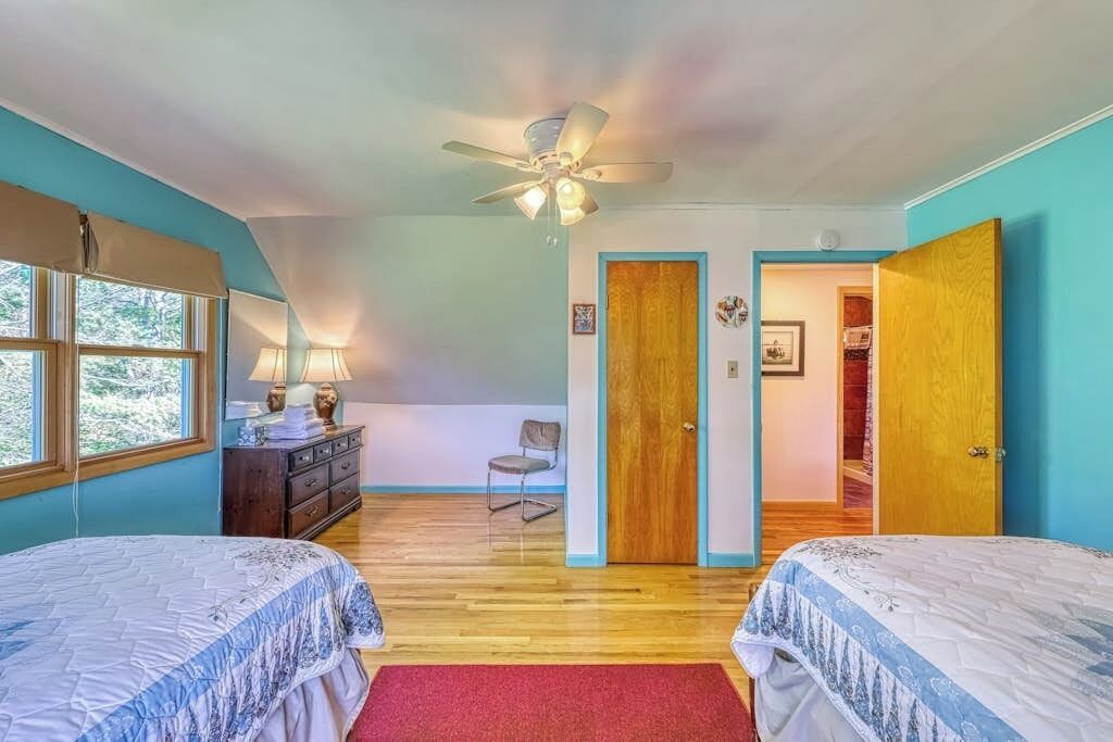 Une chambre avec deux lits, un ventilateur de plafond, une commode et une chaise.