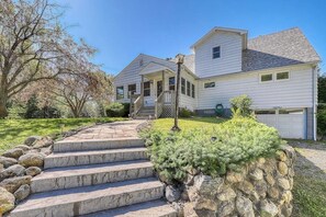 A two-story house with a stone staircase leading to the front door, surrounded by a well-maintained lawn and a large tree. - 4BR Lakefront Adirondacks - Dock (Brant Lake)