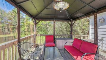 A covered outdoor seating area with a table and two red cushioned chairs, surrounded by a wooden deck and a metal railing.