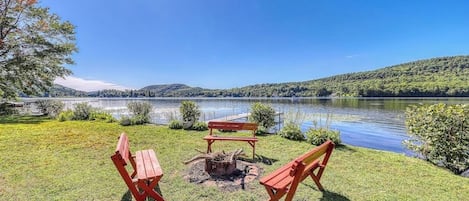 A lakeside outdoor seating area with a fire pit, benches, and a view of the lake and hills.