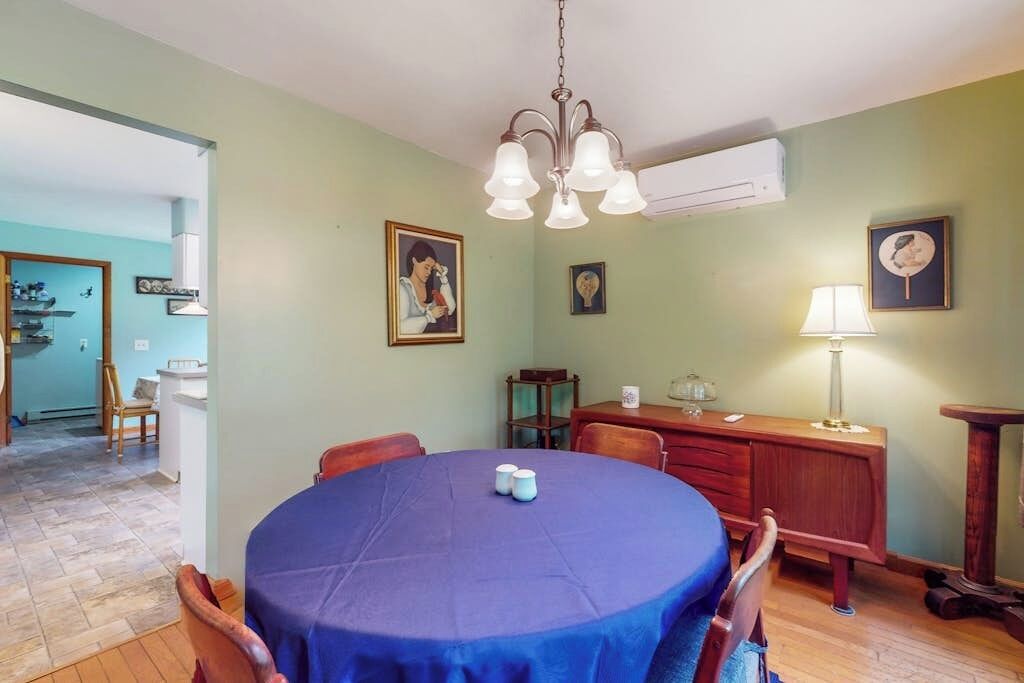 Un coin repas avec une table ronde recouverte d’une nappe bleue, des chaises en bois et un lustre.