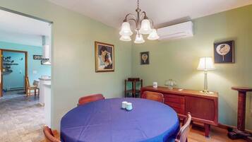 Un coin repas avec une table ronde recouverte d’une nappe bleue, des chaises en bois et un lustre.