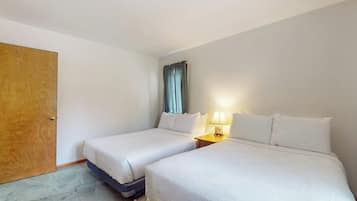 Een hotelkamer met twee bedden, een houten deur, een raam met gordijnen en een nachtkastje met een lamp.