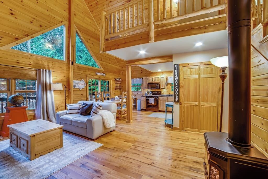 A wooden cabin interior with a living area, kitchen, and a fireplace.