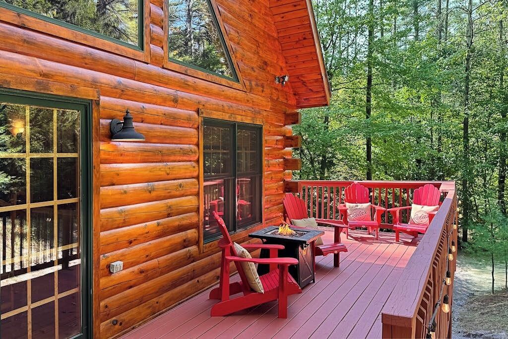 A log cabin with a deck, red Adirondack chairs, and a fire pit.