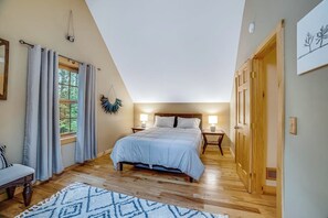 A bedroom with a large bed, a window with curtains, a wooden floor, and a door. - Child-friendly 3BR Adirondacks - Fireplace (Warrensburg)