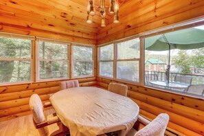 Ein Holzblock-Innenraum mit rundem Tisch und Stühlen, großen Fenstern und einer Deckenleuchte.