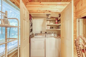 A compact laundry area with a washing machine and dryer, a small shelf with items, and a telephone on a rack. - Peaceful 3BR Lakefront Adirondacks - Dock (Brant Lake)