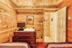 A wooden cabin room with a bed, dresser, mirror, and a door leading to another room. - Peaceful 3BR Lakefront Adirondacks - Dock (Brant Lake)