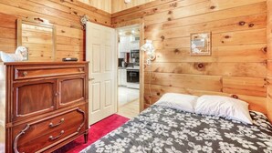 Ein Zimmer mit Holzvertäfelung, einem Bett, einer Kommode und einer Tür zu einer Küche.