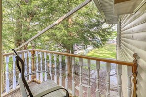 A wooden porch with a chair, white balustrade, and a view of a green landscape. - Peaceful 3BR Lakefront Adirondacks - Dock (Brant Lake)