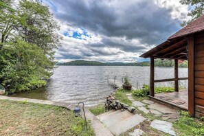 A lakeside cabin with a stone pathway leading to a wooden deck, surrounded by greenery and a view of a lake. - Beautiful 1BR Lakefront Adirondacks - Dock (Chestertown)