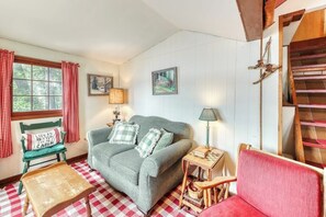 A cozy room with a checkered floor, a green sofa with plaid cushions, a red armchair, a wooden table, and a window with red curtains. - Beautiful 1BR Lakefront Adirondacks - Dock (Chestertown)