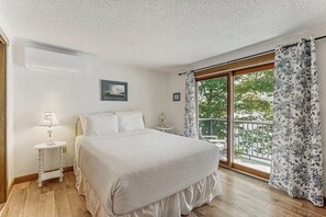Een slaapkamer met een bed, een nachtkastje, een lamp, een schilderij aan de muur en een balkon met gordijnen.