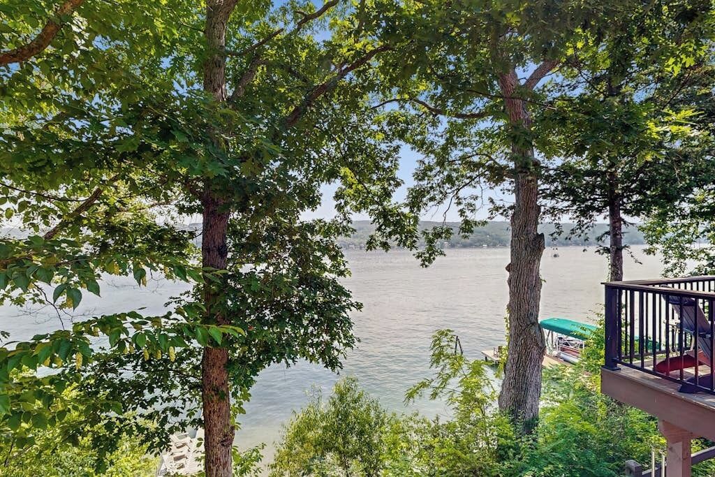 A view of a lake with trees in the foreground and a deck with a railing.