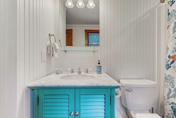 Een badkamer met een wit wastafelmeubel, blauwe kastjes, een wit toilet en een spiegel boven de wastafel.