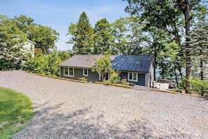 A house with a gravel driveway, a solar panel roof, and a small front yard with trees and shrubs. - Lakefront Retreat w/Private Dock & Cozy Deck Views (Penn Yan)