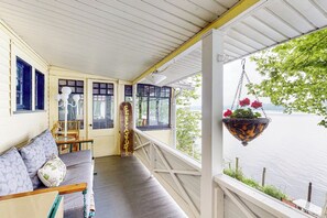 En veranda med en träbänk, en hängande blomkruka och utsikt över en sjö eller ett annat vattendrag.