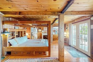 Interior de fusta amb un llit gran, armaris de fusta i una vista per una porta de vidre.