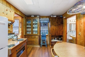 A compact kitchen with wooden cabinets, a stove, and a dining table. - Classic 2BR Riverfront Adirondacks - Deck (Chestertown)