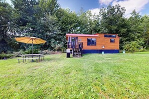 Una cabana de fusta amb teulada vermella, un petit porxo i una taula de pícnic amb una ombrel·la.
